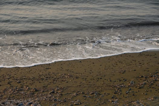 Soft waves roll onto a stony beach as dusk descends, casting a serene atmosphere by the water's edge.
