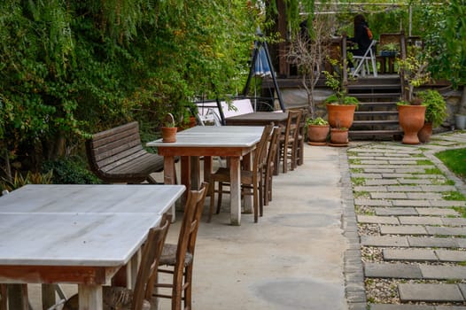 Cozy wooden tables and chairs create an inviting atmosphere among greenery, perfect for relaxing or dining outdoors.