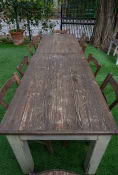 A rustic wooden table sits invitingly in a serene garden, surrounded by cozy chairs, ideal for gatherings.