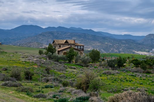 A charming house nestled in vibrant greenery, framed by rolling hills and the serene presence of towering mountains.
