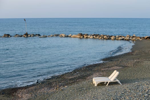 A solitary lounge chair sits on the sandy shore, overlooking tranquil waters at dusk, inviting relaxation and solitude.