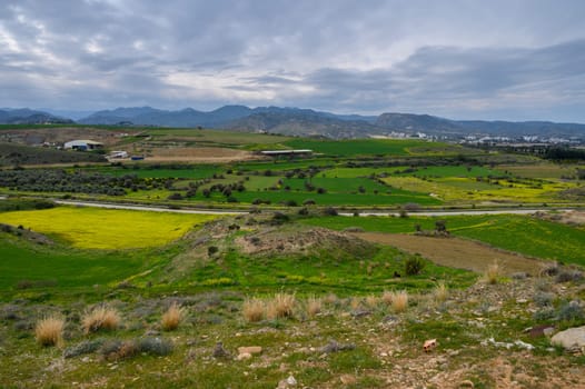 Lush green fields and farms spread across the landscape, with distant mountains looming under gray clouds.