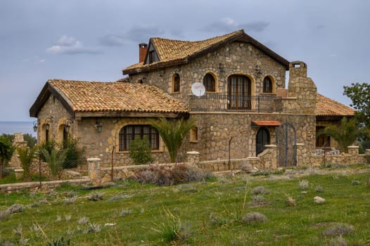 A charming stone villa is surrounded by green grass and distant hills, creating a peaceful rural retreat.