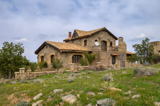 Charming villa with a rustic design sits amidst lush greenery under a cloudy sky, offering a peaceful escape.