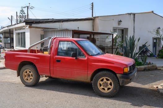 A weathered red pickup truck idle near a simple home under clear skies, evoking a peaceful, rural atmosphere.