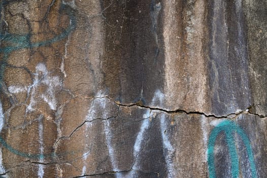 A rugged stone wall showcases unique textures, colors, and faint graffiti, telling a captivating visual story.