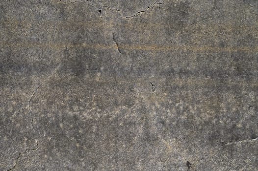 Cracks and textures create a mosaic of shadows and light on a weathered concrete surface during midday.