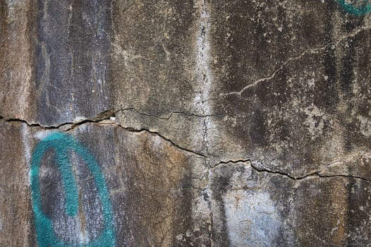 A textured stone surface bears prominent cracks and vibrant graffiti, showcasing signs of decay and urban artistry.
