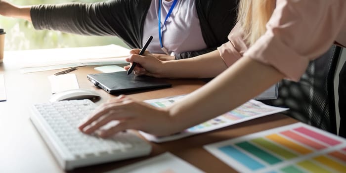 Close-up of two female graphic designers using digital tools and color palettes, highlighting teamwork and creativity in a modern office environment.
