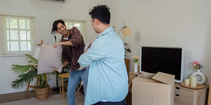 A gay couple sharing a lighthearted moment as they play with pillows while unpacking in their new home, celebrating their love and partnership.
