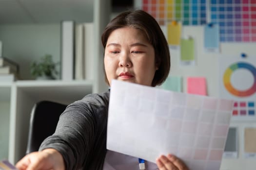A diverse graphic designer carefully selecting color swatches while focusing on a project in a bright creative environment.