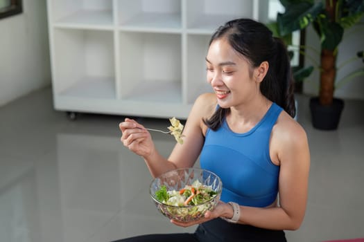 A happy woman seated on the floor savoring a delicious salad, showcasing healthy eating in a bright indoor space.