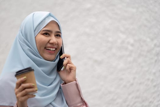 A cheerful Muslim businesswoman engages in a phone conversation, showcasing professionalism and cultural diversity in a contemporary setting.