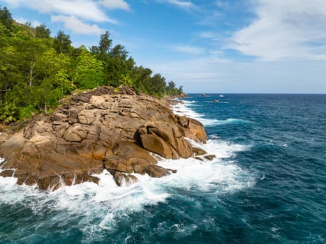 Rocks and boulders with ocean surf against a backdrop of lush tropical vegetation. Seychelles, Mahe.