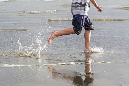 Boy runs along beach and makes splashes in the water at Pacific Beach in Washington.