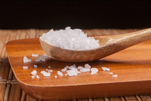 A close up image of a wooden spoon filled with sea salt on a cutting board.