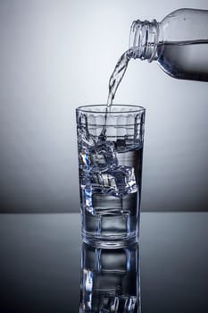 Water being poured from a bottle into a glass of ice.