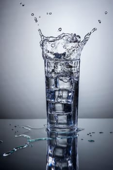 Ice being dropped into a glass of water making a splash.