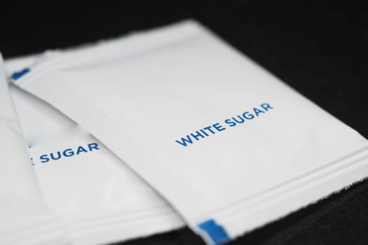 White sugar packets are neatly arranged on a dark surface ready for use.