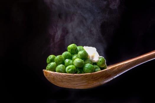 Peas topped with butter on a wooden spoon with steam from below.