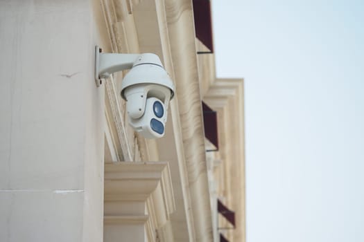 A security camera is fixed to the side of a building under a clear sky.