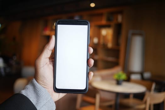 A person presents a smartphone with a blank screen in a stylish cafe.