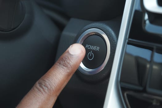A hand is pressing the power button in a car dashboard.