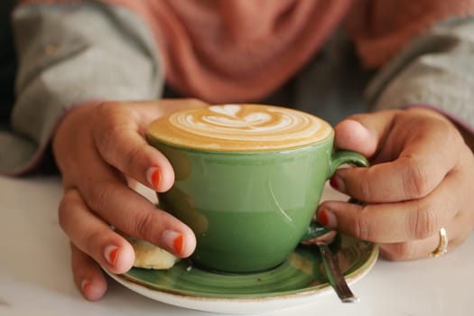 Warm coffee cup held by hands with colorful nail polish in a cafe .