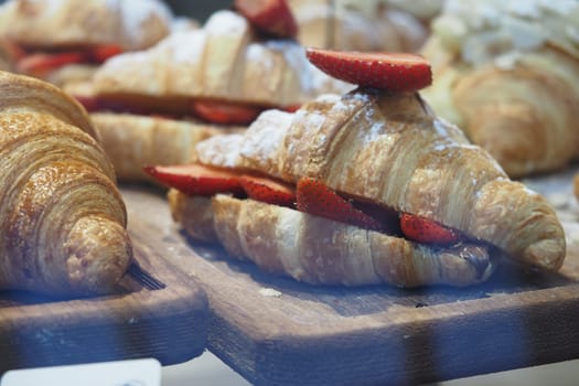 Delicious croissants filled with fresh strawberries sit on a wooden board.