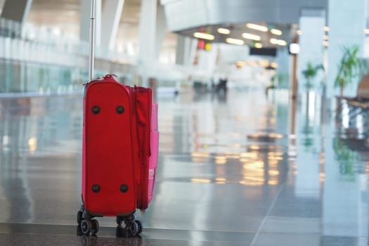A bright red suitcase is positioned in an empty airport terminal.