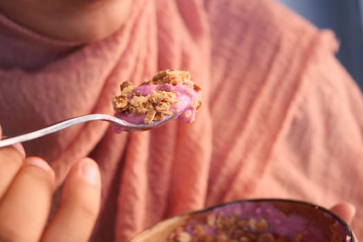 Individual takes a spoonful of yogurt topped with granola outdoors.