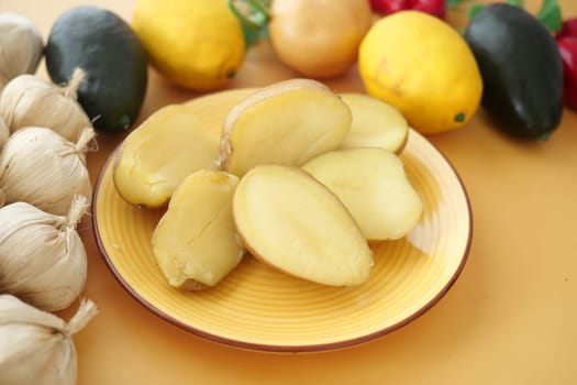 Cut potatoes placed on a yellow plate with vibrant vegetables nearby.