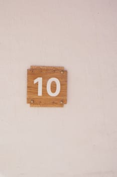 Wooden number 10 sign attached to a plain wall, minimalistic style.
