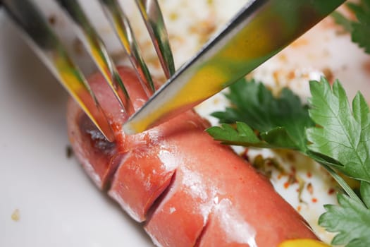 A close-up of a fork and knife slicing through a sausage with herbs.