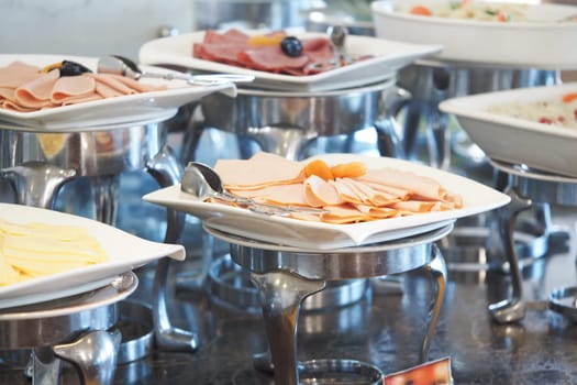 Several plates of cold cuts and salads are arranged on a buffet table.