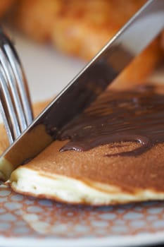 A fork and knife slice through a delicious pancake with chocolate spread.