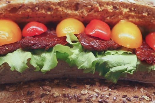 Vibrant vegetable toppings on a hearty sandwich against wood.