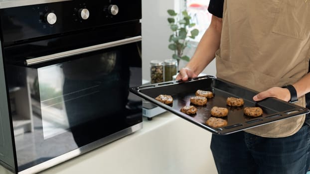 Young man holding a baking tray filled with chocolate chip cookie dough, ready to bake.