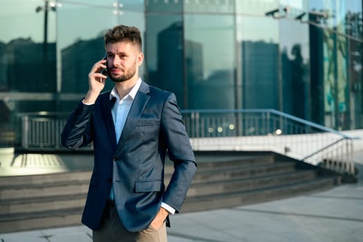 Bearded businessman talking on mobile phone outside office building.