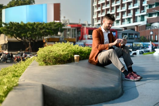Handsome businessman using mobile phone while sitting outside in a public space.