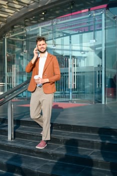Stylish businessman having phone conversation while walking out of office building.