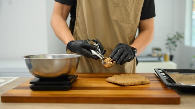 Baker wearing black gloves scooping chocolate chip cookie dough onto a baking tray.