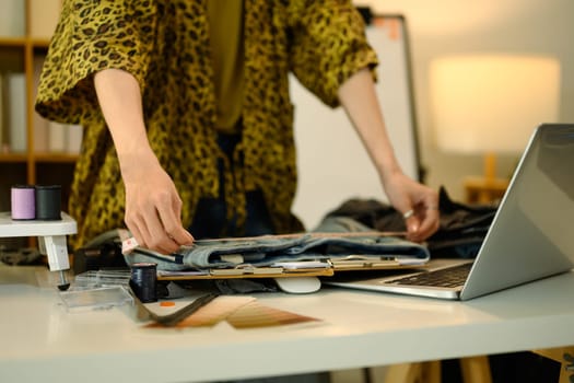 Young designer measuring denim jacket with tape measure in a creative fashion studio.