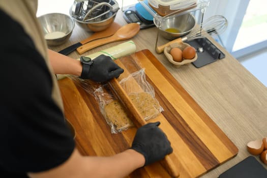 Baker rolling out cookie dough on a wooden board.
