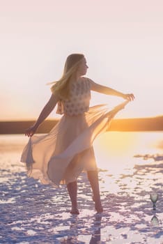 Slender girl stands on the surface of sea salt at sunset. She is illuminated by the setting sun. Her chiffon dress is illuminated. Her silhouette on the horizon. Kuyalnik, Odessa, Ukraine