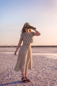 blonde girl stands in the middle of a salt lake. her dress flutters in the wind. the surface is pink. she has a bouquet in her hands, she covers her face. kuyalnik, odessa.