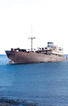 A rusted ship rests abandoned in calm blue waters, evoking mystery and nostalgia.