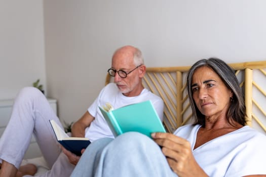 Mature caucasian woman reading book at home. Couple relaxing in bedroom. Lifestyle concept.