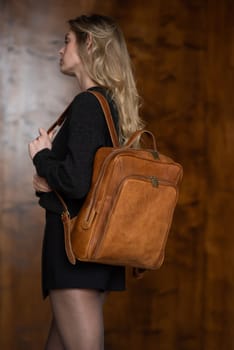 A girl in a warm sweater, a black short skirt and nylon tights is posing with a light brown backpack