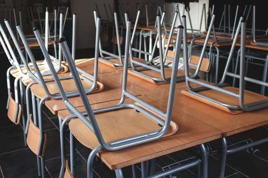 This image captures a classroom setting where chairs are stacked upside down on top of tables, creating an organized yet empty atmosphere, emphasizing a moment of silence.